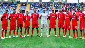 **Alt Text:** Rangers International FC players pose for a team photo before a Nigeria Premier Football League match, wearing their traditional red kits on the pitch in Enugu.