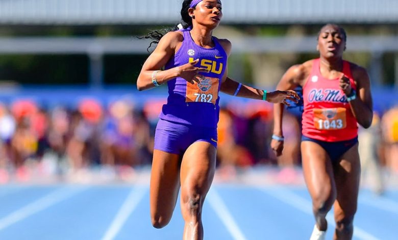Tima Godbless crossing the finish line first in her 200m heat at the SEC Outdoor Championships, arms extended in victory and determination on her face.