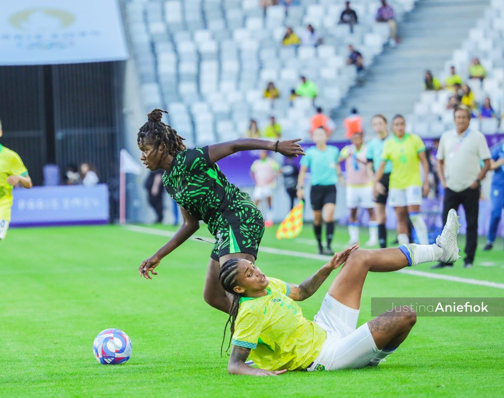 Esther Okoronkwo, dressed in the green and white jersey of the Super Falcons, controls the ball during an intense match, showcasing her composure and focus.